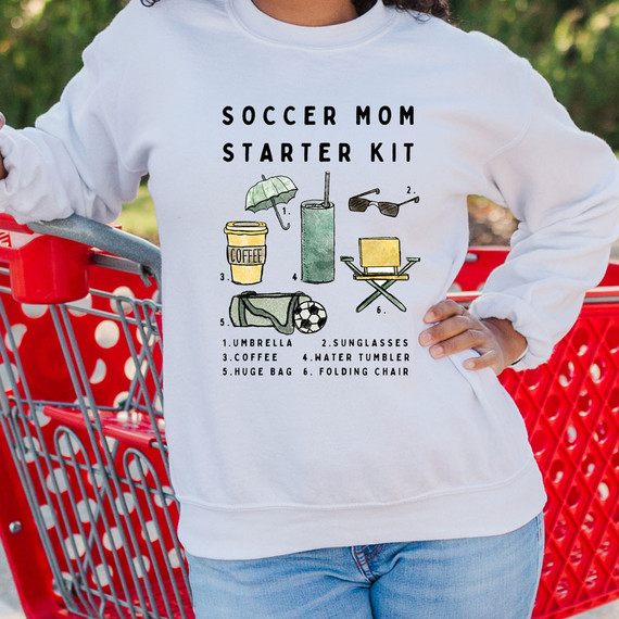 Soccer Mom Starter Kit DTF Heat Transfer, illustration of items like umbrella, sunglasses, coffee, water tumbler, huge bag, and folding chair on a white sweatshirt.