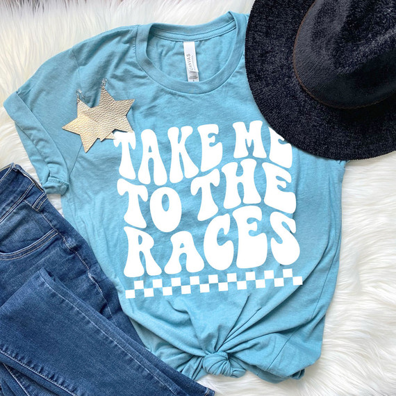 Take Me To The Races WHITE DTF Heat Transfer, white text on a light blue T-shirt with checkered pattern at the bottom, styled with a denim jeans, a black hat, and a star-shaped earrings.