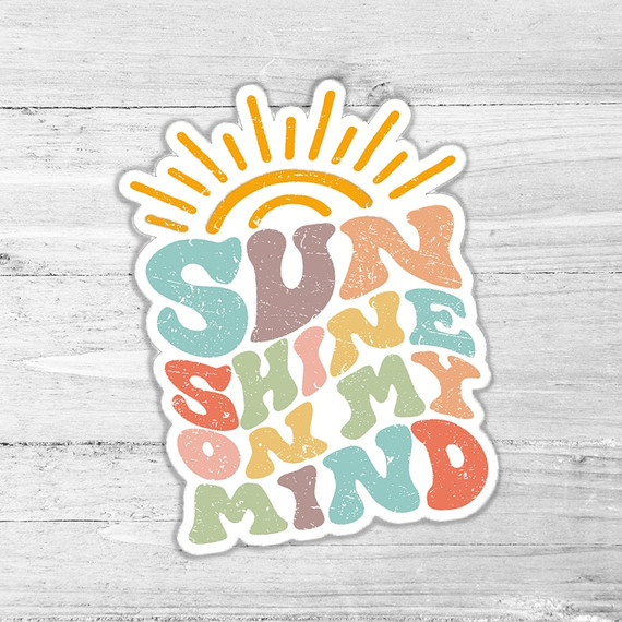 Sunshine On My Mind Die Cut Sticker, colorful cut-out sticker featuring the phrase 'Sunshine On My Mind' with a sun illustration at the top, on a light wooden background.