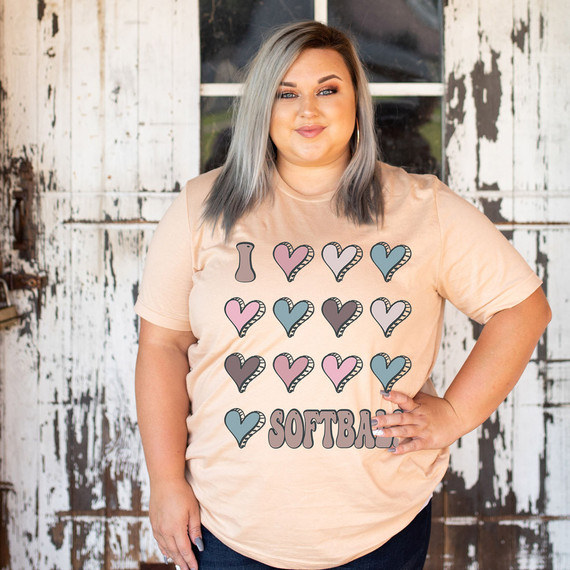 I Love Softball Hearts Heat Transfer, woman wearing beige T-shirt with heart-shaped softball graphics in pink, blue, gray colors, and the word SOFTBALL in block letters.