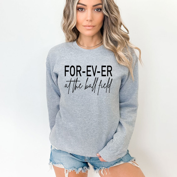 For-Ev-Er At The Ball Field DTF Heat Transfer, image of a woman wearing a gray sweatshirt with 'FOR-EV-ER at the ball field' printed on it.