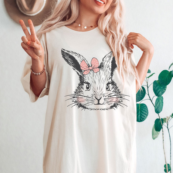 Bunny With Pink Bow DTF Heat Transfer, a cute bunny face with a pink bow on its head printed on a cream t-shirt.