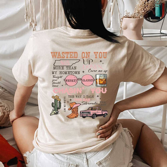 Wallen Titles DTF Heat Transfer, image of a woman wearing a beige t-shirt with a colorful, decorative design with text and images like whiskey glasses, a cactus, cowboy boots, and a pink pickup truck.