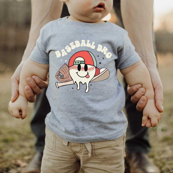 Baseball Bro Retro DTF Heat Transfer, a colorful cartoon design of a smiling baseball with a face, cap, baseball bat, and glove, printed on a child's t-shirt.