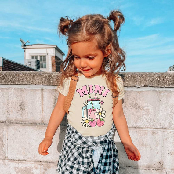 Mini Spring Drinks DTF Heat Transfer, image of a young girl wearing a t-shirt with a colorful spring-themed drink design featuring a jar, flowers, and strawberries.