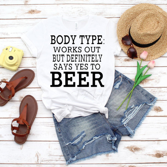 Body Type Works Out But Definitely Says Yes To Beer Sublimation Transfer T-shirt on a flat lay with sunglasses, straw hat, tulips, denim shorts, sandals, and a yellow camera on a white wooden background.