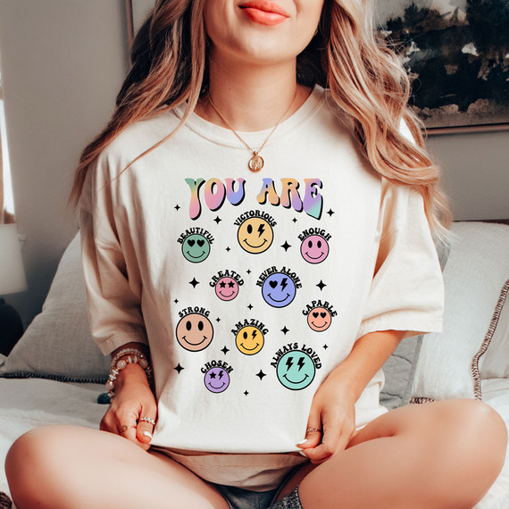 You Are Happy Faces VERSION 2 DTF Heat Transfer, colorful design of smiling faces with positive affirmations on a white t-shirt worn by a woman.