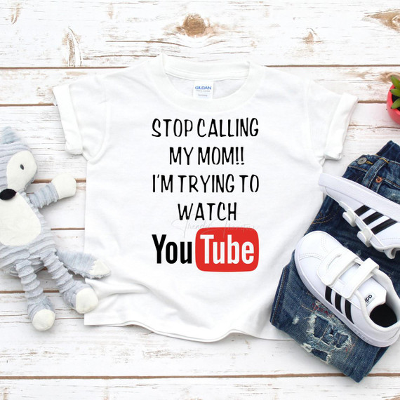 Stop Calling My Mom I'm Trying To Watch YouTube Sublimation Transfer T-shirt, white graphic tee with humorous text and YouTube logo on a white wooden background.