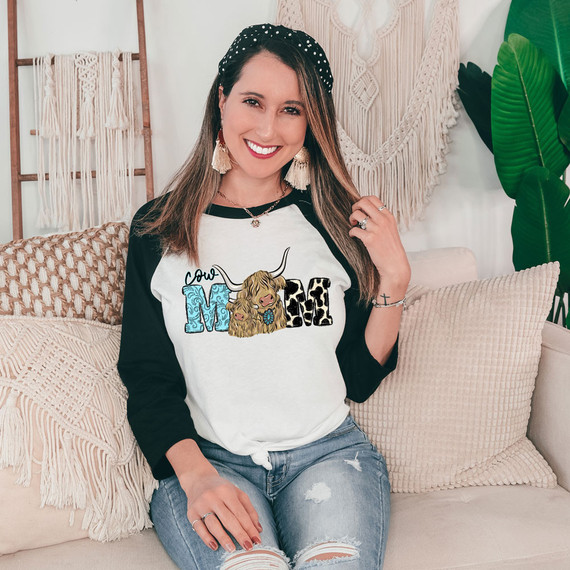 Cow Mom DTF Heat Transfer, a woman sitting on a beige couch wearing a stylish baseball tee with cow-themed graphic design.