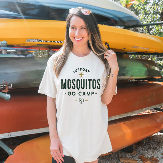 Support Mosquitos Go Camp DTF Heat Transfer, a design for outdoor camping and mosquito support on a white T-shirt worn by a smiling woman near kayaks.