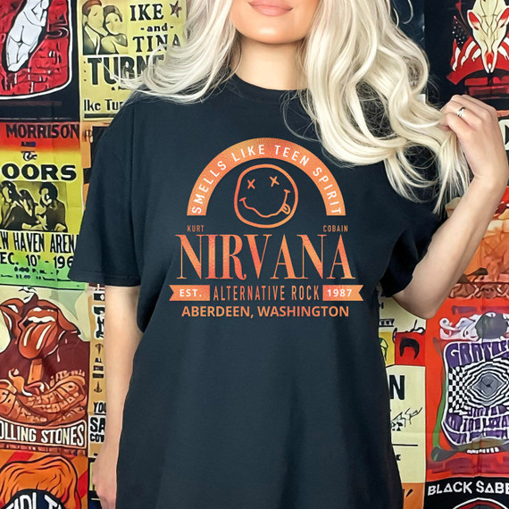 Band Tee NV DTF Heat Transfer, Coral-colored design featuring Nirvana band logo, smiley face with crossed-out eyes, and band details from Aberdeen, Washington, on a black t-shirt worn by a woman with blonde hair.