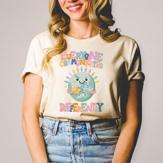 Everyone Communicates Differently DTF Heat Transfer, colorful graphic design of a globe with cartoon figures and the text Everyone Communicates Differently on a woman's t-shirt.