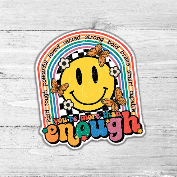 You're More Than Enough Die Cut Sticker, colorful rainbow, smiley face, butterflies, and empowering words on a wooden surface.