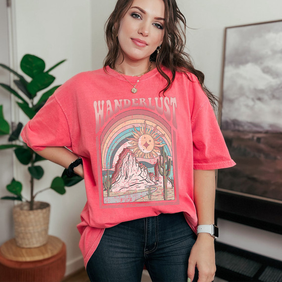 Wanderlust DTF Heat Transfer, vibrant pink graphic t-shirt with a colorful desert landscape, mountains, cacti, and a sun with a face, designed for customizing clothing and apparel.