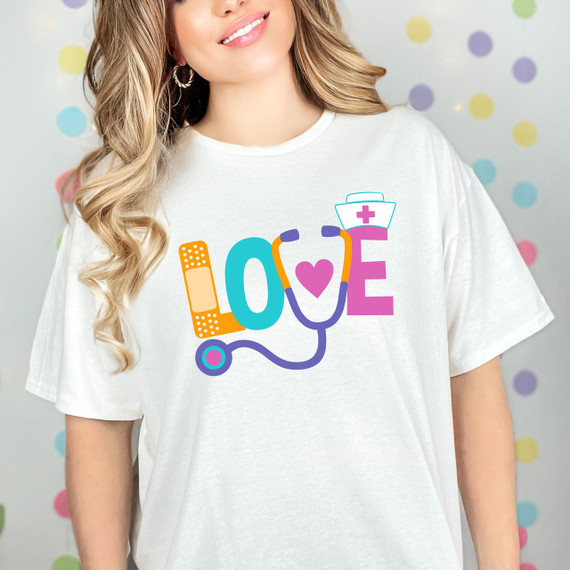 LOVE Nursing DTF Heat Transfer, colorful medical-themed design featuring a stethoscope forming the letter 'O', a bandage, and a nurse's cap with a pink cross, printed on a white T-shirt.