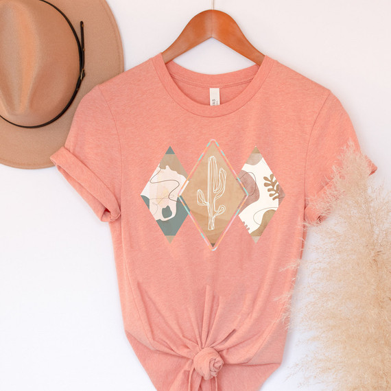Boho Diamonds Western DTF Heat Transfer, a colorful diamond-shaped desert cactus design on a pink t-shirt with a beige hat nearby.