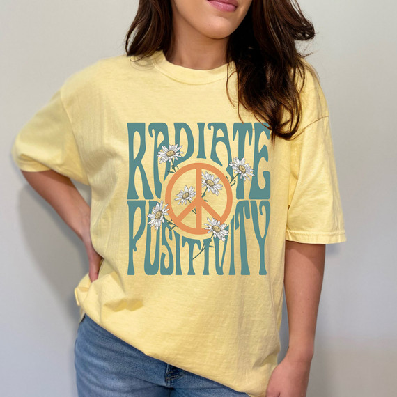 Radiate Positivity DTF Heat Transfer, yellow t-shirt with a peace sign surrounded by daisies and the words 'Radiate Positivity' in bold letters.