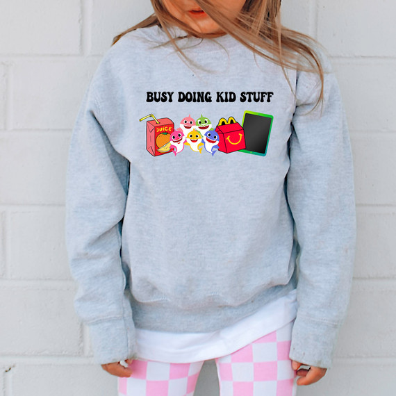 Busy Doing Kid Stuff Sharks DTF Heat Transfer, colorful cartoon sharks and kids' snacks graphic design on a girl's gray sweatshirt.