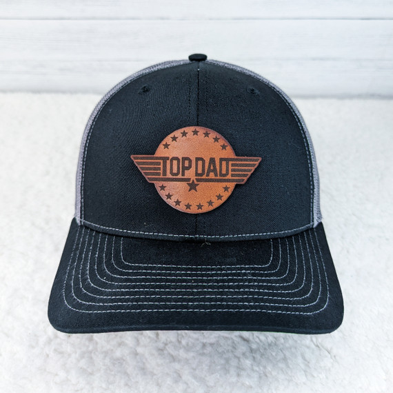 Top Dad Leather Hat Patch, a brown leather patch with wing design and stars, embroidered on a black and grey baseball cap.