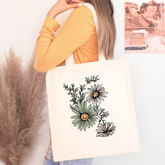 Daisies DTF Heat Transfer, floral design on a canvas tote bag held by a woman wearing an orange striped long sleeve shirt.
