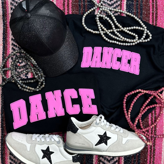 Dancer Pink Youth Screen Print Heat Transfer, black t-shirts with pink DANCER heat transfer design, paired with gray and black sneakers, pink and gray pearl necklaces, and a black cap with glitter, on a pink and black striped background.