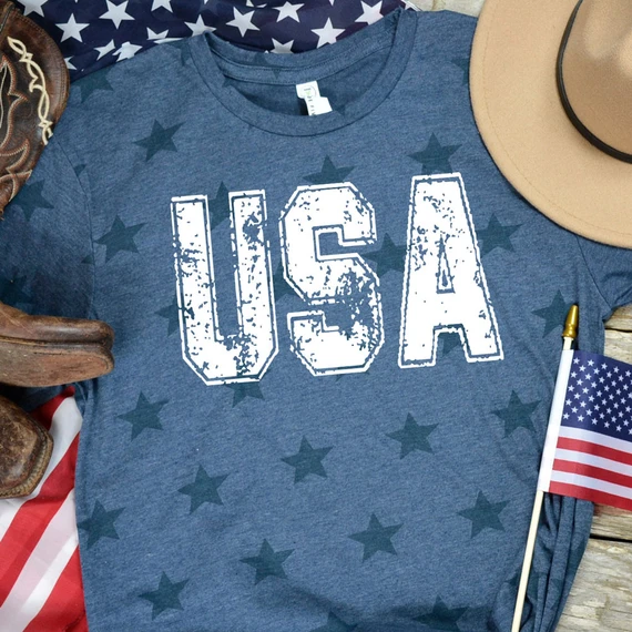 USA Distressed DTF Heat Transfer, blue T-shirt with distressed USA lettering, American flag, and patriotic accessories for a patriotic theme.