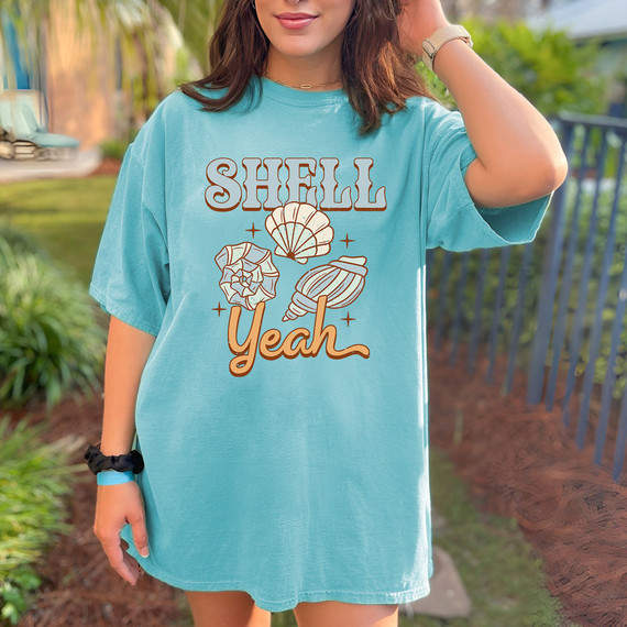 Shell Yeah DTF Heat Transfer, woman wearing a blue t-shirt with a seashell design and the text 'SHELL Yeah' printed on it.