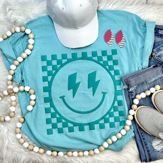 Checkered Happy Face TEAL GREEN PUFF Screen Print Heat Transfer, teal green t-shirt with a happy face design featuring electrical bolt eyes and checkered background, surrounded by fashion accessories.