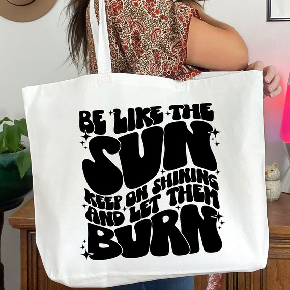 Be Like The Sun BLACK DTF Heat Transfer, a black and white tote bag with a motivational quote in bold, playful font.