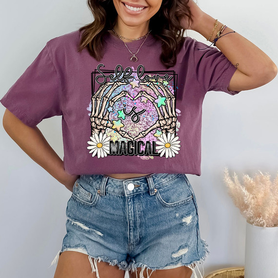 Self Love Is Magical DTF Heat Transfer, colorful and whimsical design featuring skeleton hands forming a heart with stars and daisies, on a purple T-shirt.