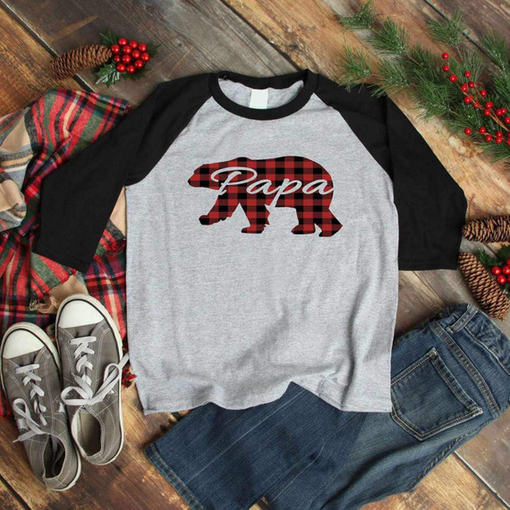 Papa Bear Buffalo Plaid Sublimation T-shirt, gray and black raglan shirt with a buffalo plaid bear graphic and 'Papa' text, styled with casual jeans, sneakers, and surrounded by holiday decorations on a wooden surface.
