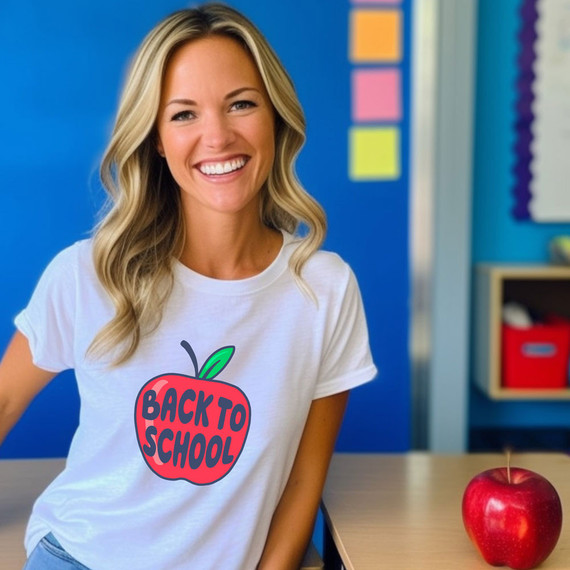 Back To School Apple DTF Heat Transfer, a woman wearing a white t-shirt with a colorful apple design and the words "Back To School" printed on it, smiling in a classroom setting.