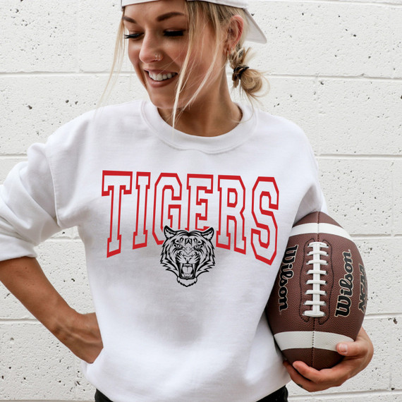 Tigers Red DTF Heat Transfer, woman wearing a white sweatshirt with a tiger graphic and the word 'TIGERS' in red, holding a football.
