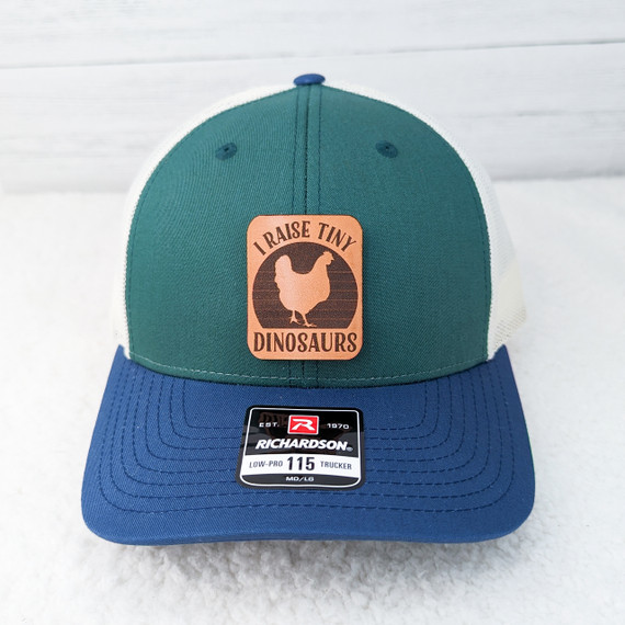 I Raise Tiny Dinosaurs Leather Hat Patch, embroidered patch featuring a dinosaur silhouette with the text 'I Raise Tiny Dinosaurs' on a peach background.