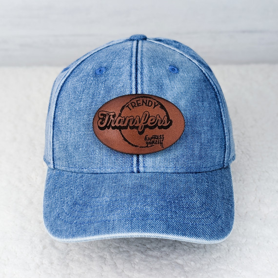 Custom Leather Hat Patch, a brown leather patch with black embroidered text and design, attached to a blue denim baseball cap.
