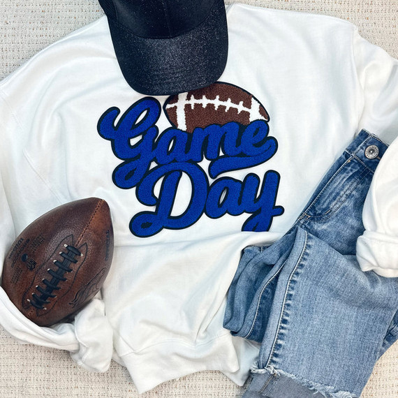 Royal Game Day Football Chenille Patch, with a football design and blue lettering, placed on a white sweatshirt alongside a black cap, a football, and denim jeans.