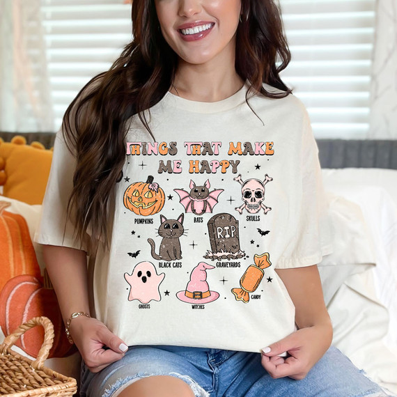 Things That Make Me Happy Spooky DTF Heat Transfer, a colorful Halloween-themed design featuring pumpkins, bats, skulls, black cats, gravestones, ghosts, witches, and candy on a woman's T-shirt.
