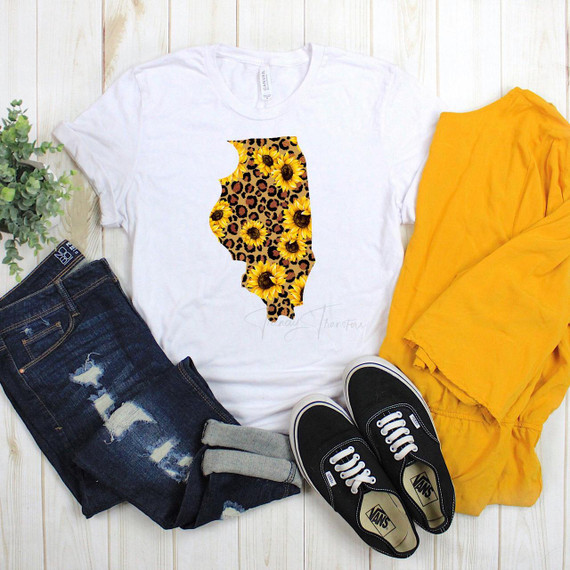 Illinois Leopard Sunflower Sublimation Transfer, white t-shirt with sunflower and leopard print Illinois state design, surrounded by denim jeans, yellow jacket, black Vans shoes, and green plant on white wooden background.
