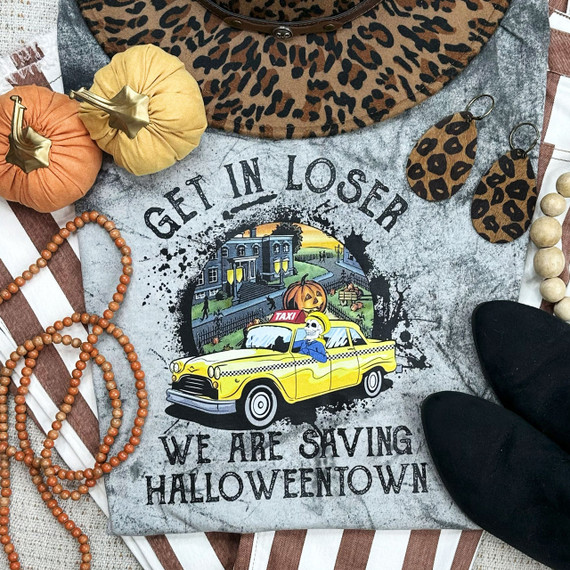 Get In Loser We Are Saving Halloween Screen Print Heat Transfer, Halloween themed T-shirt with a yellow taxi and skeleton driver, surrounded by pumpkins and Halloween decorations.