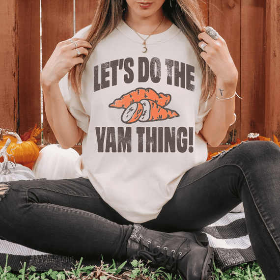Let's Do The Yam Thing DTF Heat Transfer, a woman wearing a customized T-shirt with a carrot graphic and fun text, sitting outdoors with pumpkins in the background.
