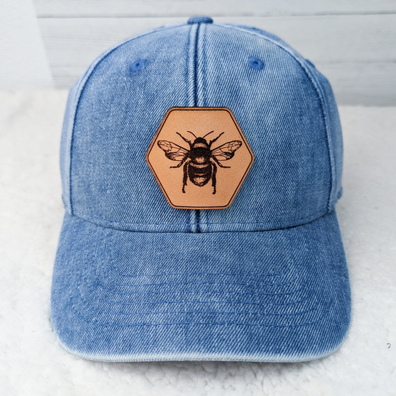 Bee Leather Hat Patch, a leather hexagon-shaped patch featuring a detailed illustration of a bee, mounted on a blue denim cap.