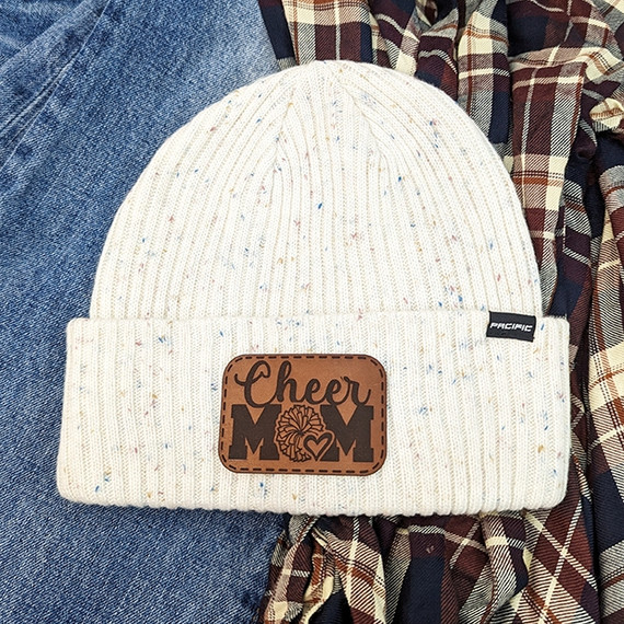 Cheer Mom Leather Hat Patch, cream-colored knit beanie with speckles and a brown leather patch featuring 'Cheer Mom' text and a cheerleading pom-pom graphic.