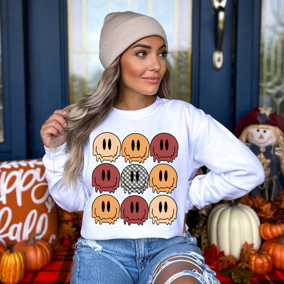 Fall Happy Faces DTF Heat Transfer, a woman wearing a white sweatshirt with colorful pumpkin and skull graphic design for fall or Halloween celebration.