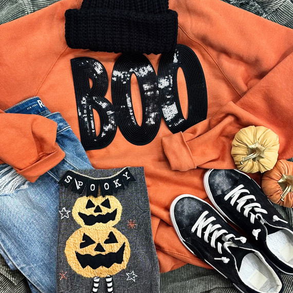 Black BOO Sequin Patch, a shiny black sequin patch spelling 'BOO' on an orange sweatshirt surrounded by Halloween-themed decor including a spooky pumpkin bag, black and white sneakers, and orange fabric pumpkins.