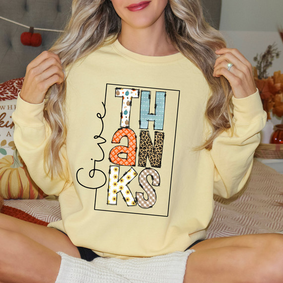 Give Thanks Patchwork DTF Heat Transfer, festive fall-themed design with colorful patchwork letters spelling 'THANKS' and 'give' in script on a yellow sweatshirt.