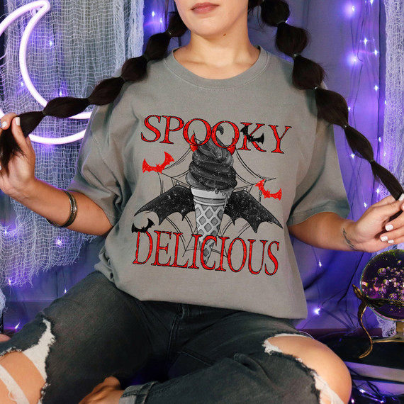 Spooky Delicious DTF Heat Transfer, halloween-themed T-shirt featuring an ice cream cone with bat wings and spooky text with purple Halloween lights in the background.