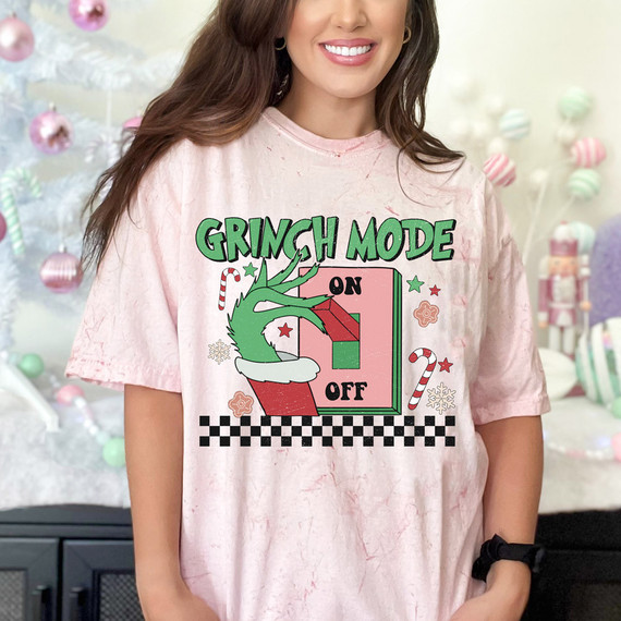 Green Guy Mode DTF Heat Transfer, woman wearing a light pink T-shirt with a Christmas-themed design featuring a green figure, Christmas candy canes, and festive elements.