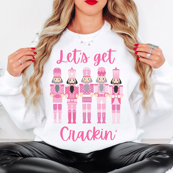 Let's Get Crackin' Pink Nutcrackers DTF Heat Transfer, a woman wearing a white sweatshirt with pink nutcracker graphic and text for festive holiday crafting.