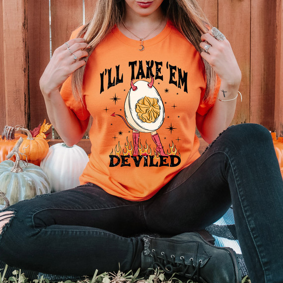 I'll Take 'Em Deviled DTF Heat Transfer, orange T-shirt with a devil-themed design of a deviled egg with red horns and legs, and flames at the bottom.