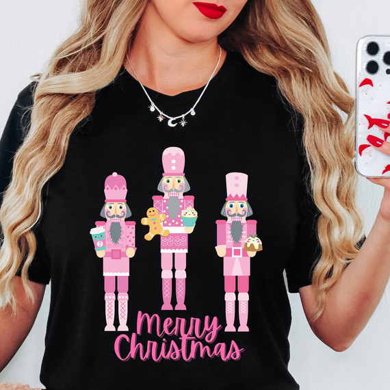 Merry Christmas Pink Nutcrackers DTF Heat Transfer, pink nutcracker characters with Christmas treats and the text Merry Christmas in pink on a black T-shirt.